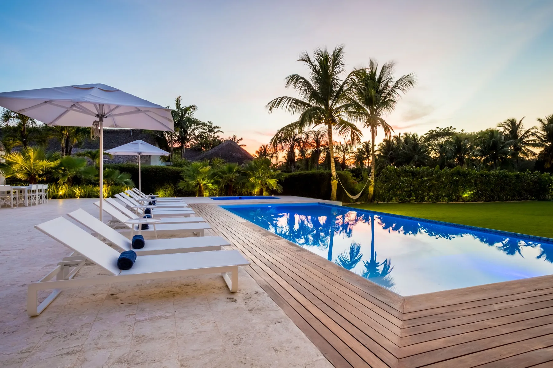 Una piscina al aire libre junto a una terraza de madera y tumbonas al atardecer.