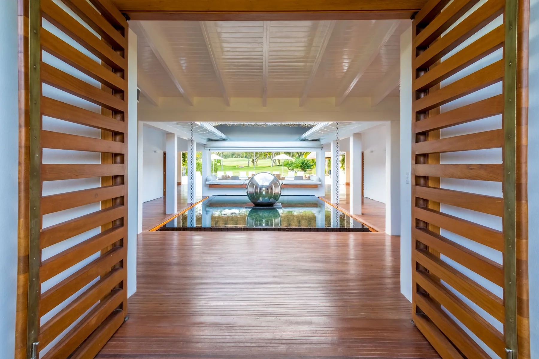 Un pasillo interior luminoso se abre hacia un elemento de agua y vegetación.