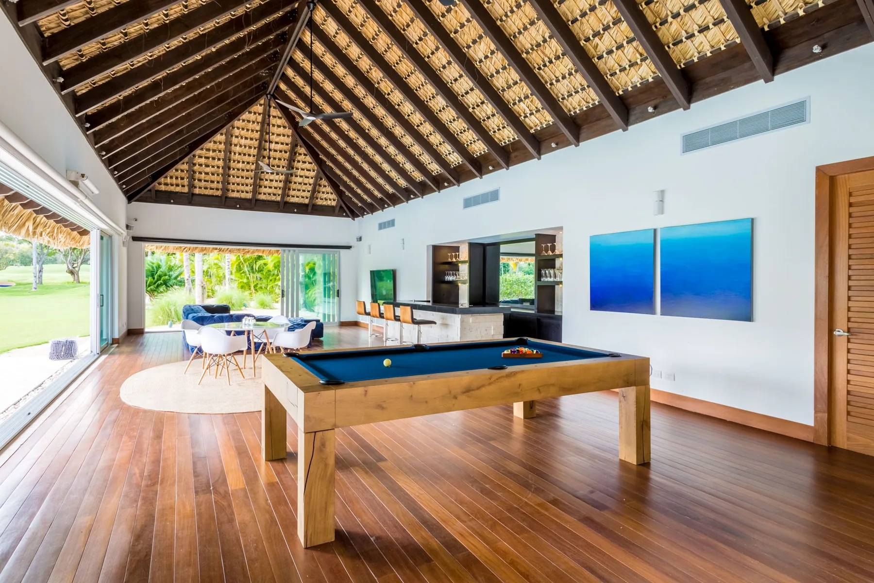Una luminosa sala de recreación con una mesa de billar y un comedor bajo un techo alto de madera.