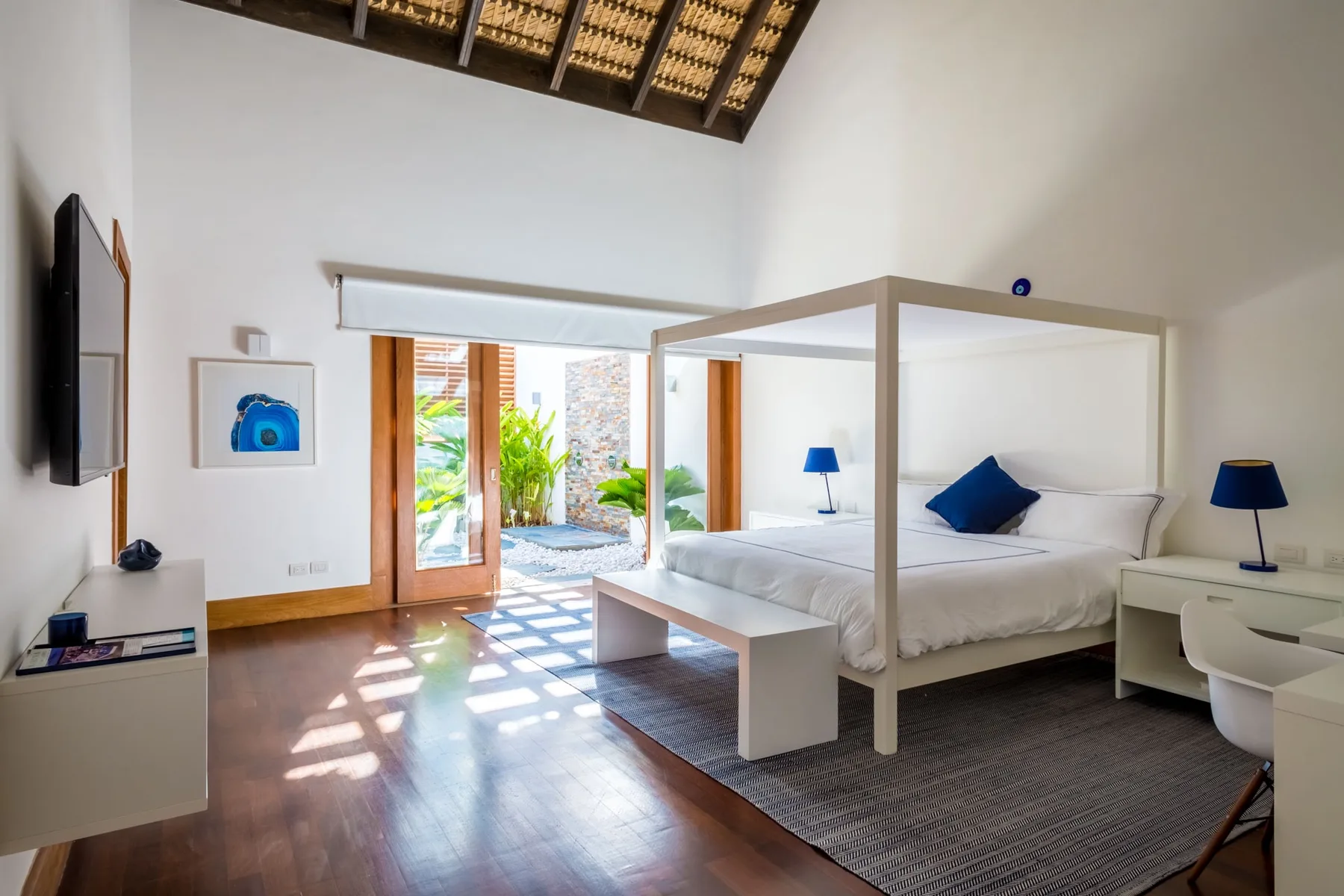 Un dormitorio luminoso con una cama con dosel blanca junto a puertas abiertas al jardín.