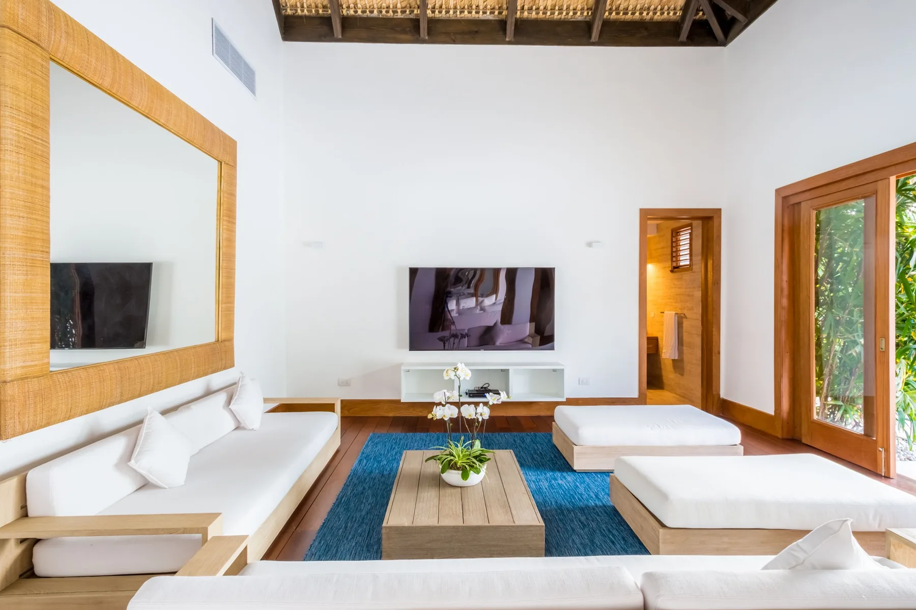 Sala de estar luminosa con televisión, asientos bajos y una ventana amplia.