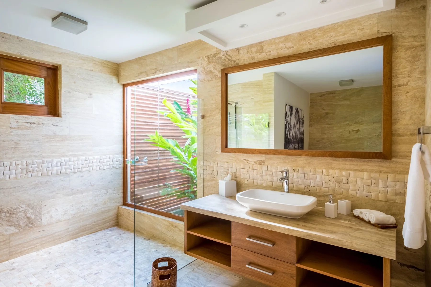 Un baño luminoso con un espejo amplio y un lavabo junto a una ducha de vidrio.
