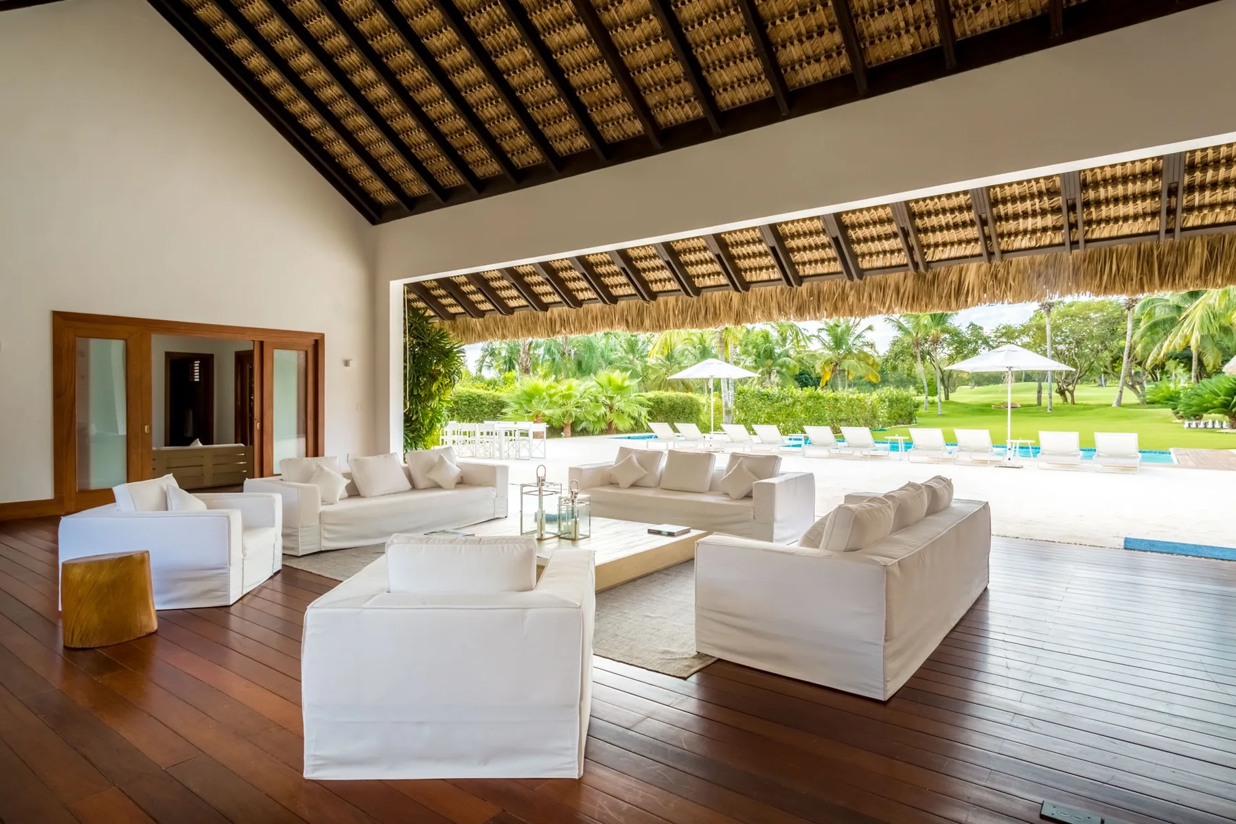 Una sala abierta con asientos blancos da a un jardín y una piscina.