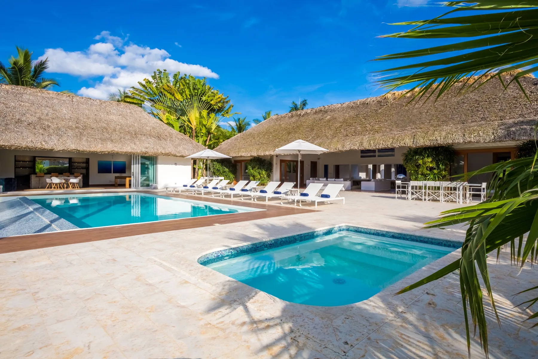 Una zona de piscina soleada con asientos junto a edificios con techo de paja.
