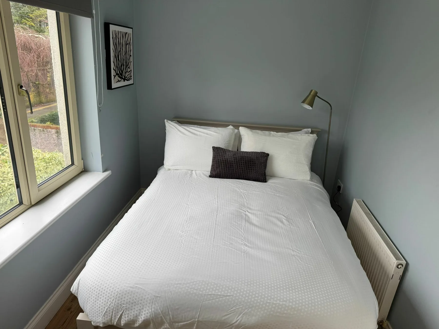 A bedroom with a neatly made bed beside a large window.