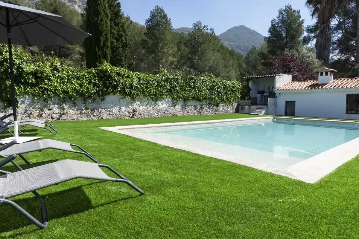 An outdoor swimming pool beside a grassy lawn and reclining loungers.