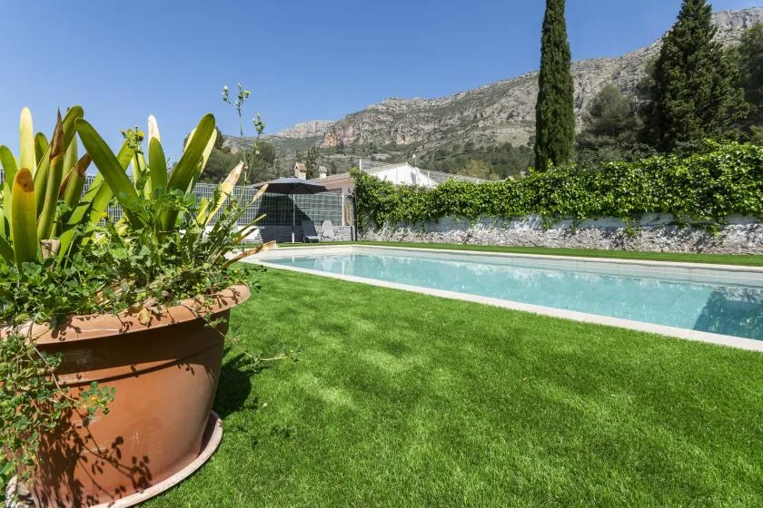 An outdoor swimming pool beside a grassy lawn, with mountains in the background.