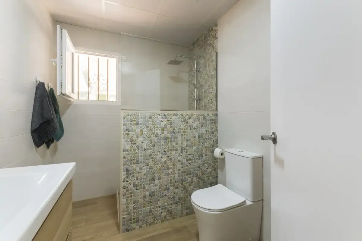 A bathroom with a shower, toilet, and bathtub beside a small window.
