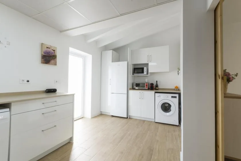 A bright kitchen with white cabinets, a refrigerator, and a washing machine.