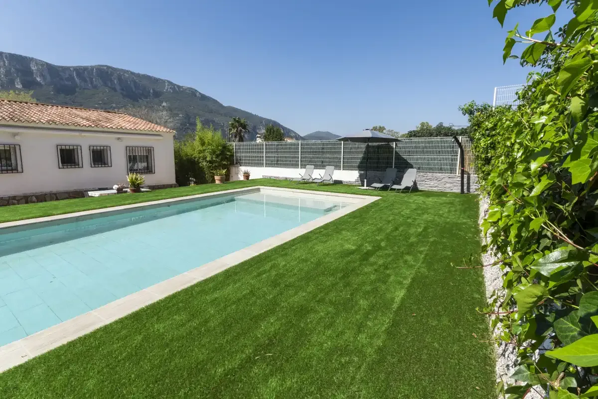An outdoor swimming pool beside a green lawn, with mountains in the background.