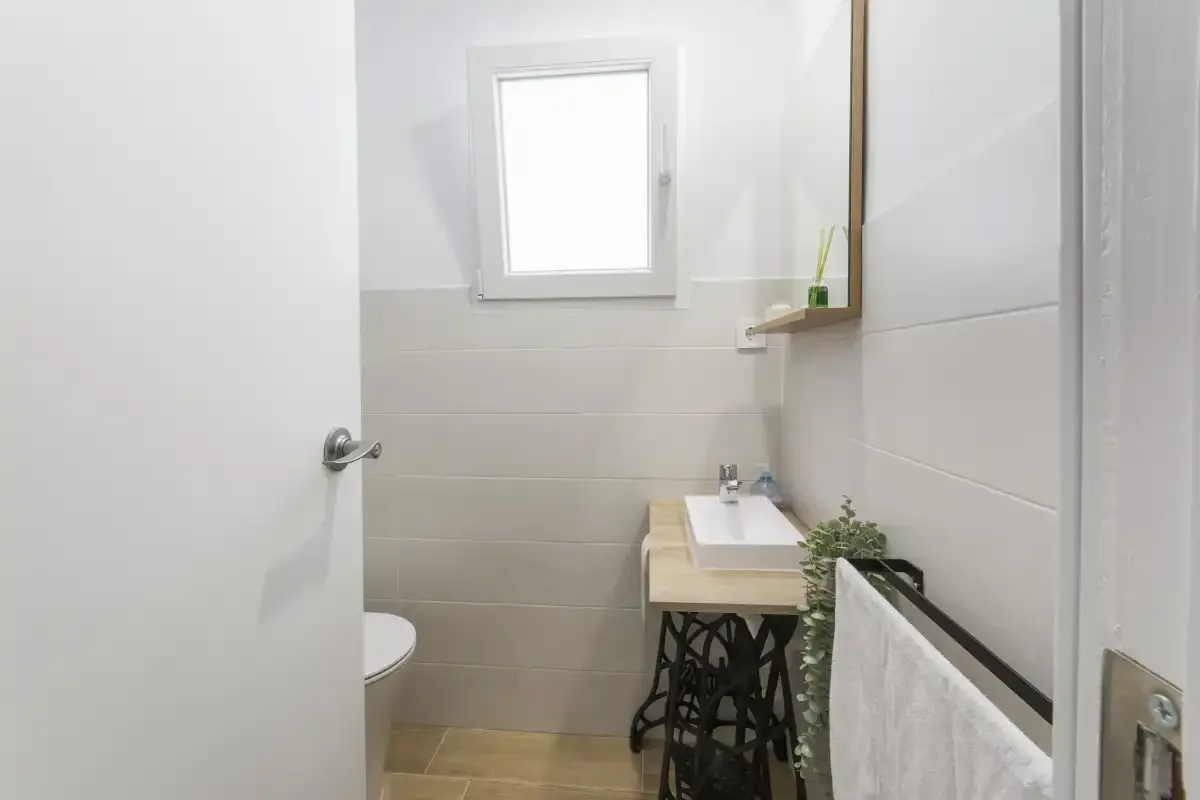A bright bathroom with a sink, toilet, and small window.