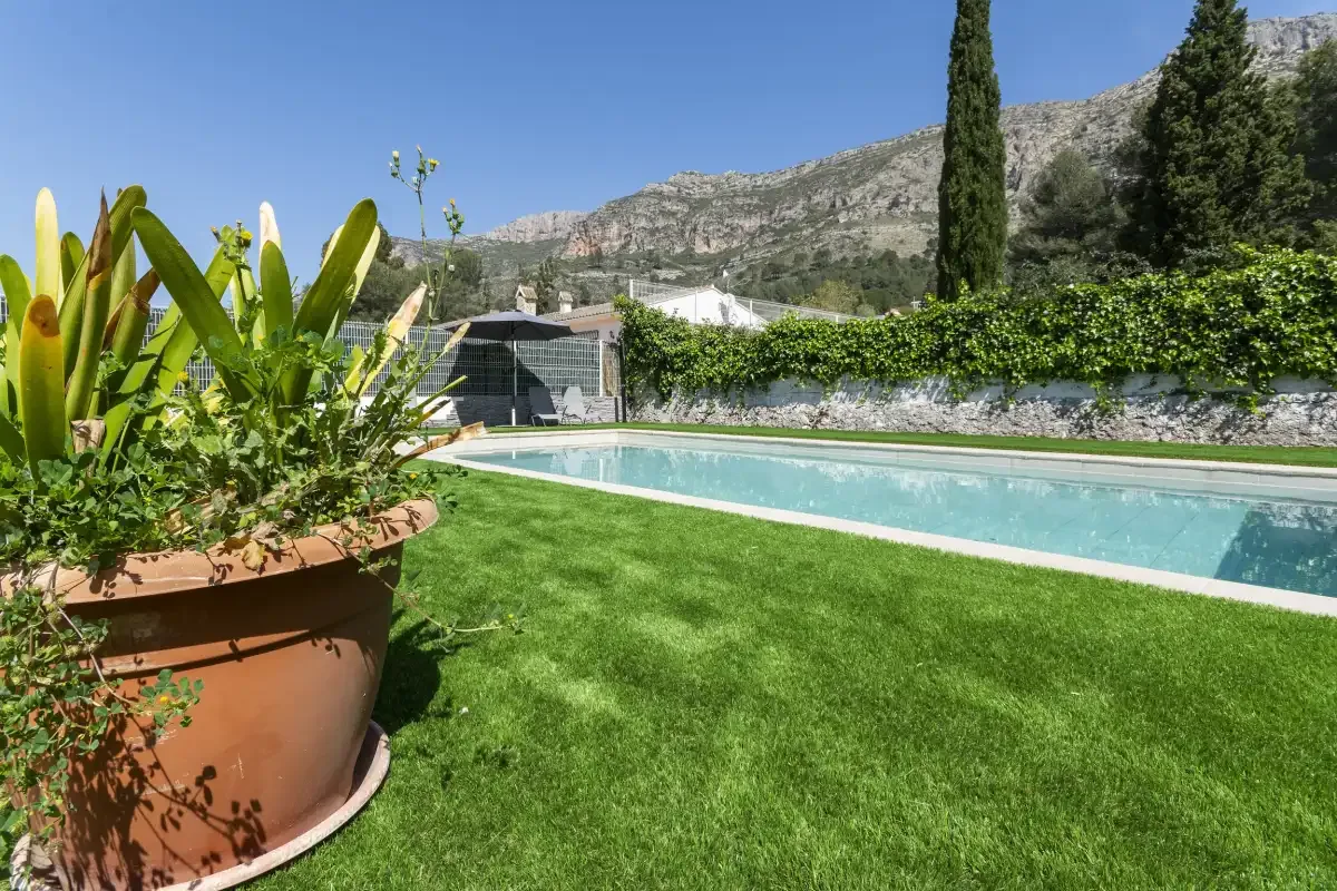 An outdoor swimming pool borders a green lawn, with mountains in the background.