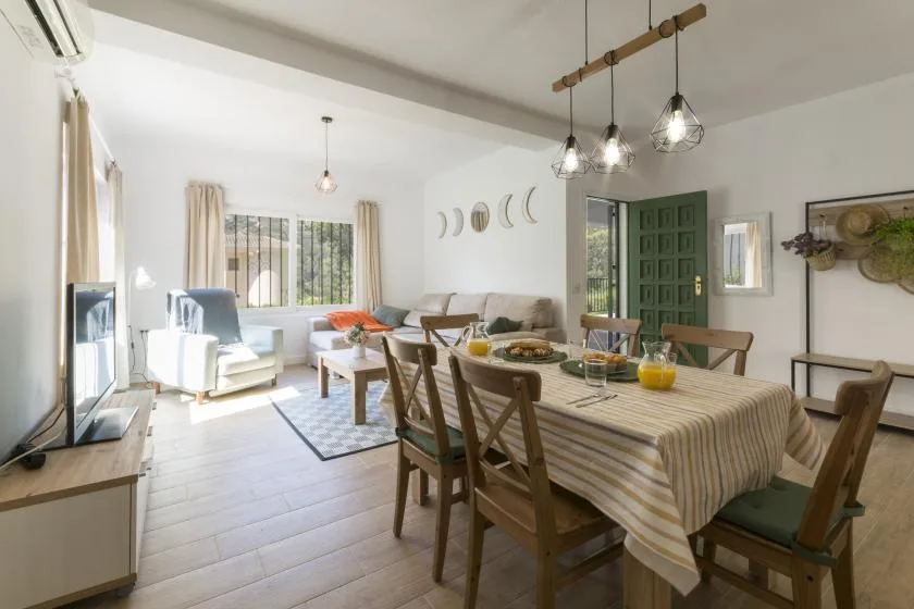 A bright living and dining area features a long table and seating by the windows.