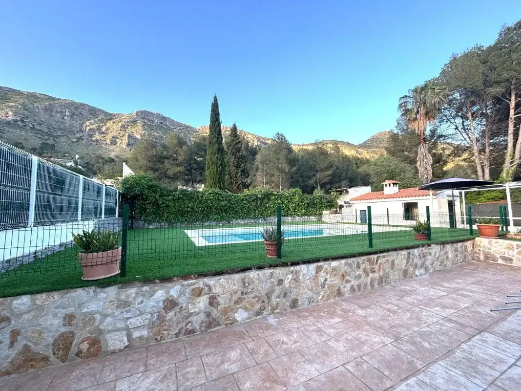 An outdoor swimming pool sits beside a paved patio, with hills in the background.