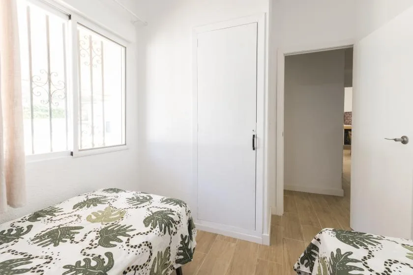 A bright bedroom with two beds and a window with decorative bars.