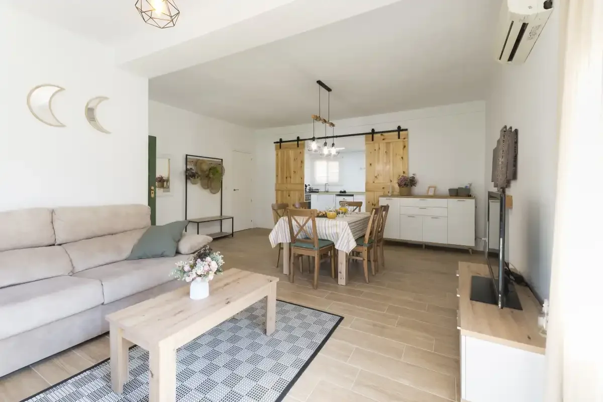 A bright living and dining room with a table, seating, and pale wood cabinetry.