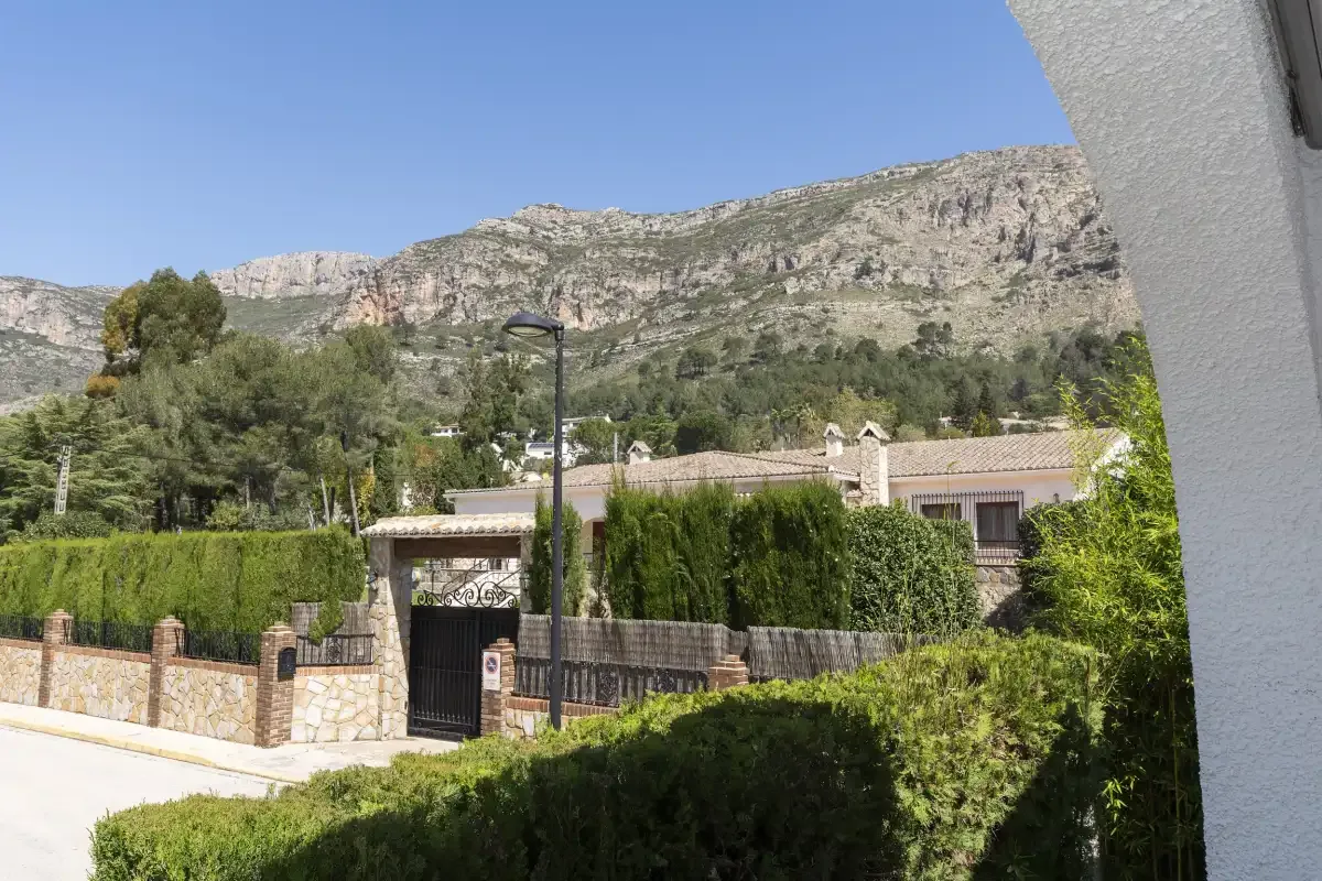 A landscaped residential property sits below a rocky mountain ridge.