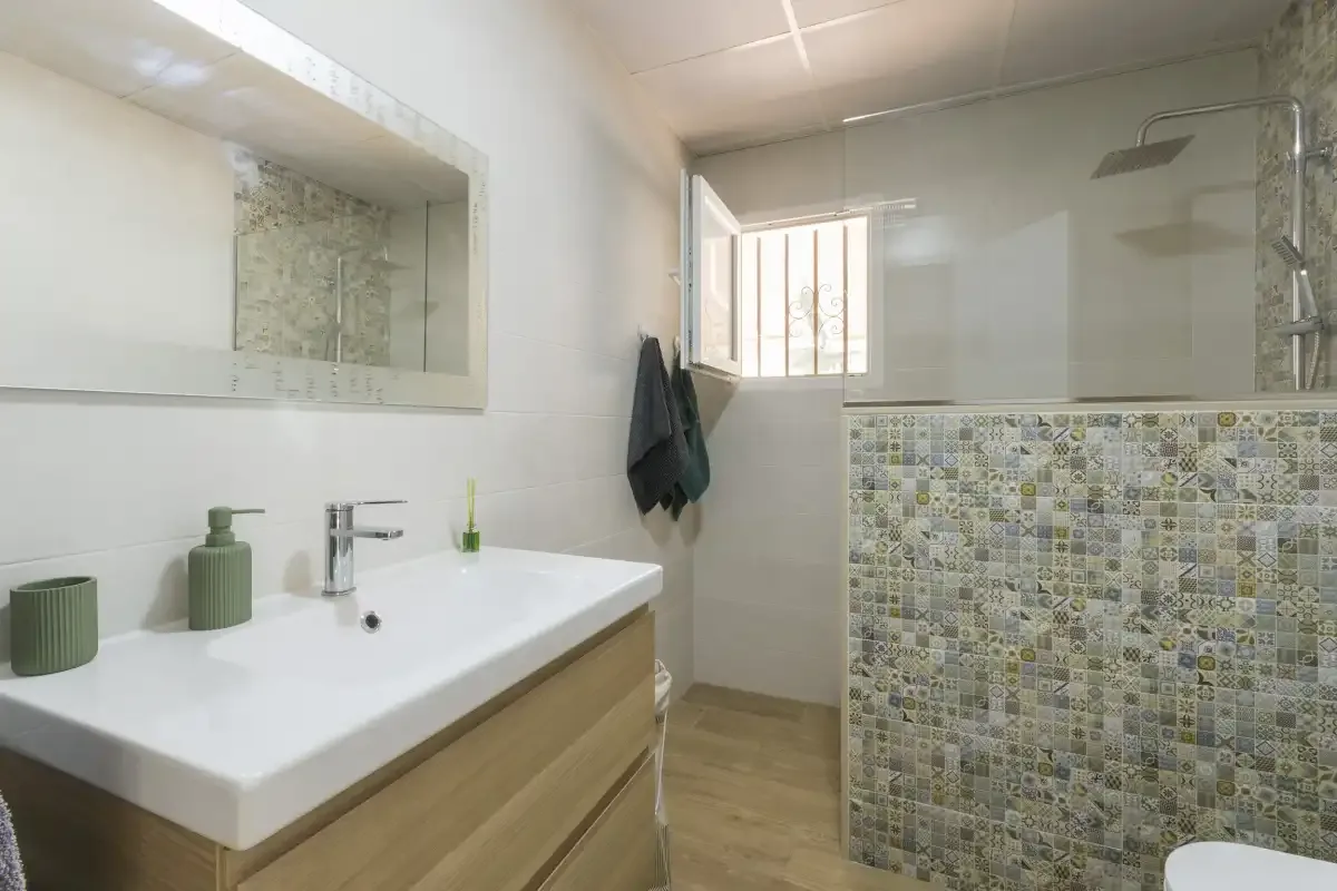 A bathroom with a sink, mirror, and tiled shower area.