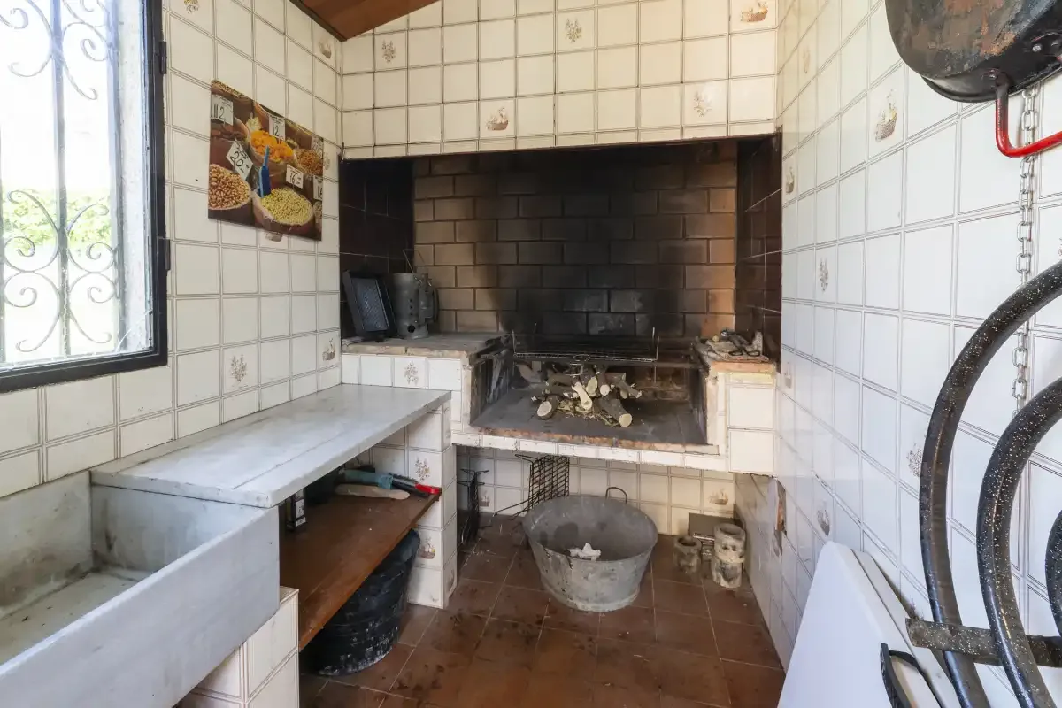 A tiled kitchen area with a large brick hearth and a metal basin.