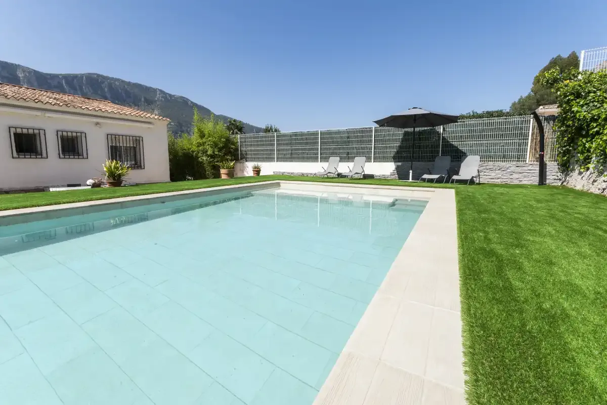 An outdoor swimming pool beside a lawn, with lounge seating at the far end.