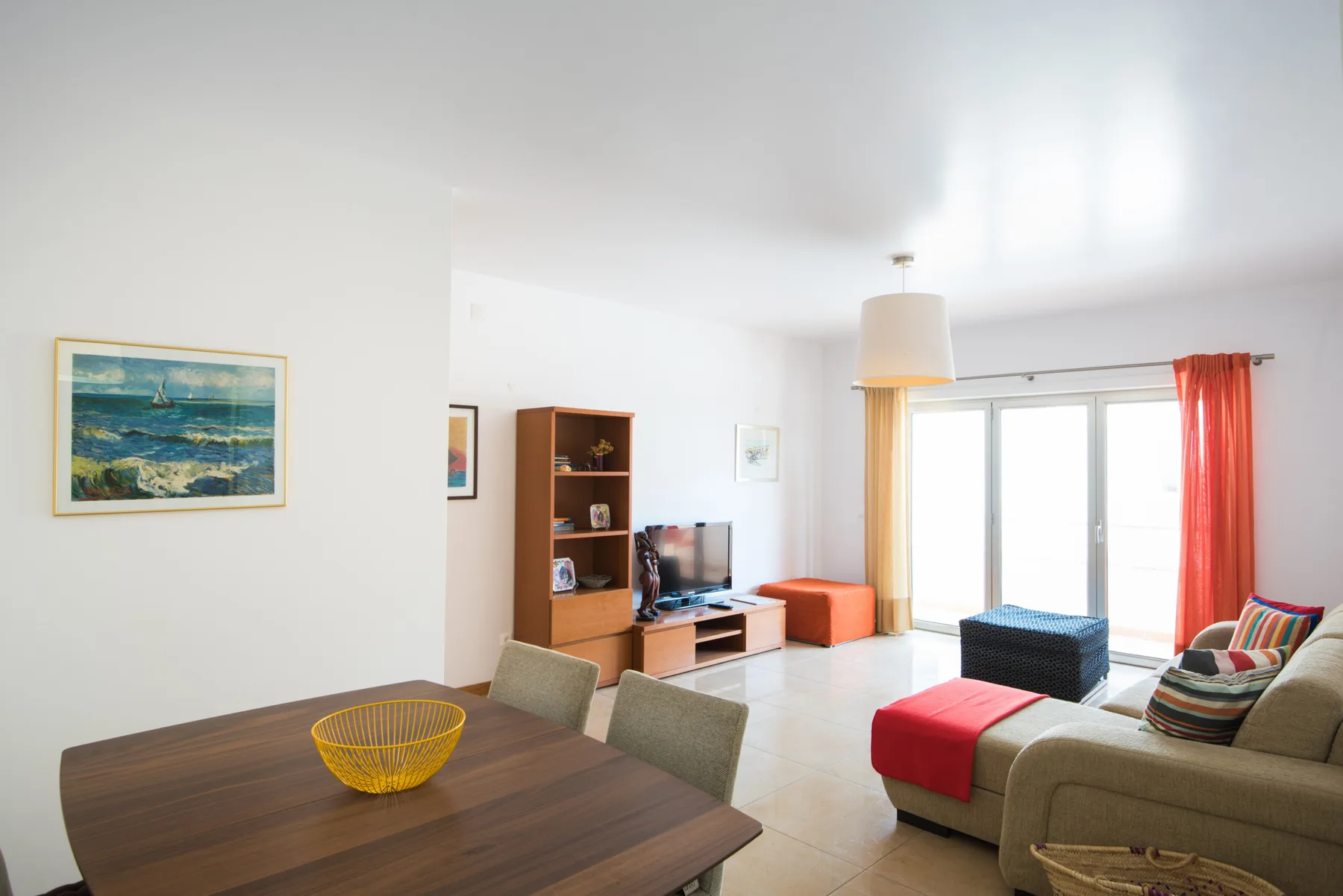 Una sala de estar y comedor luminosa, con televisor y asientos junto a las ventanas.