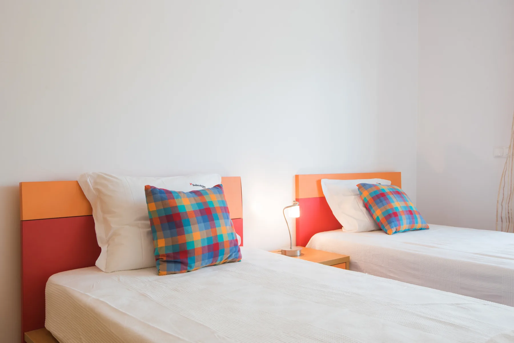 A bedroom with two beds, white bedding, and colorful plaid pillows.