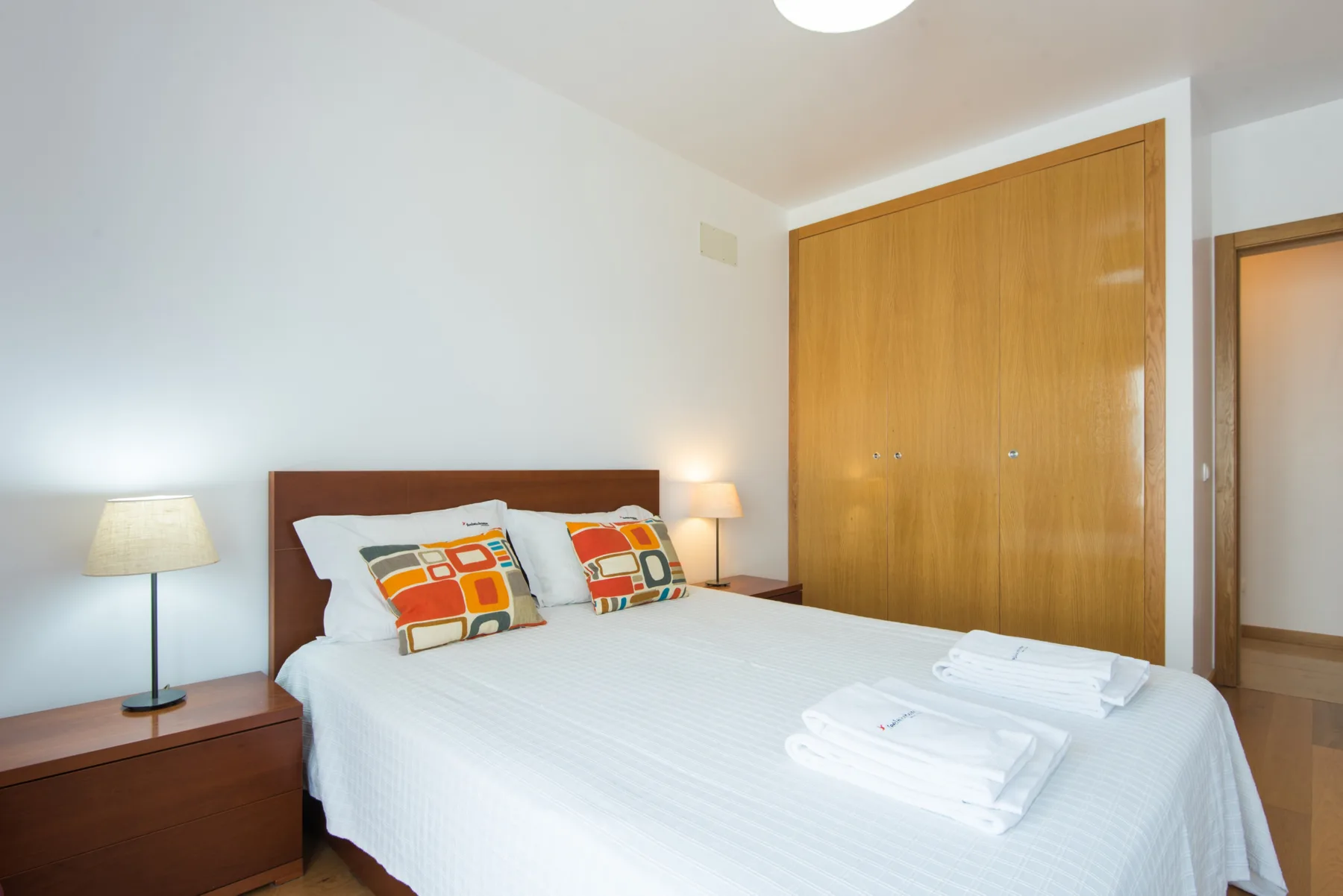 A bedroom with a neatly made bed and wooden wardrobe.