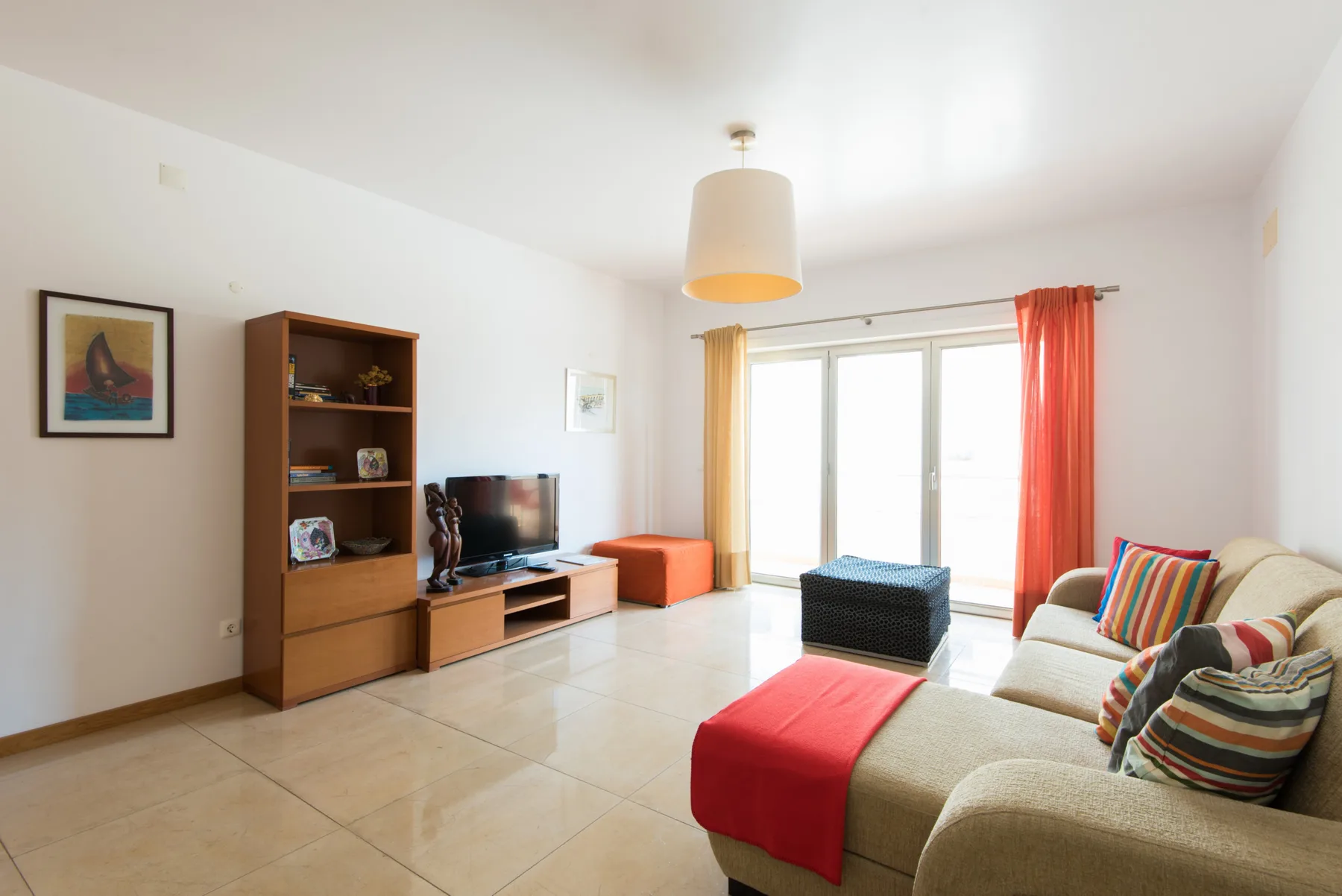 A bright living room with seating, a television, and glass doors opening to a balcony.