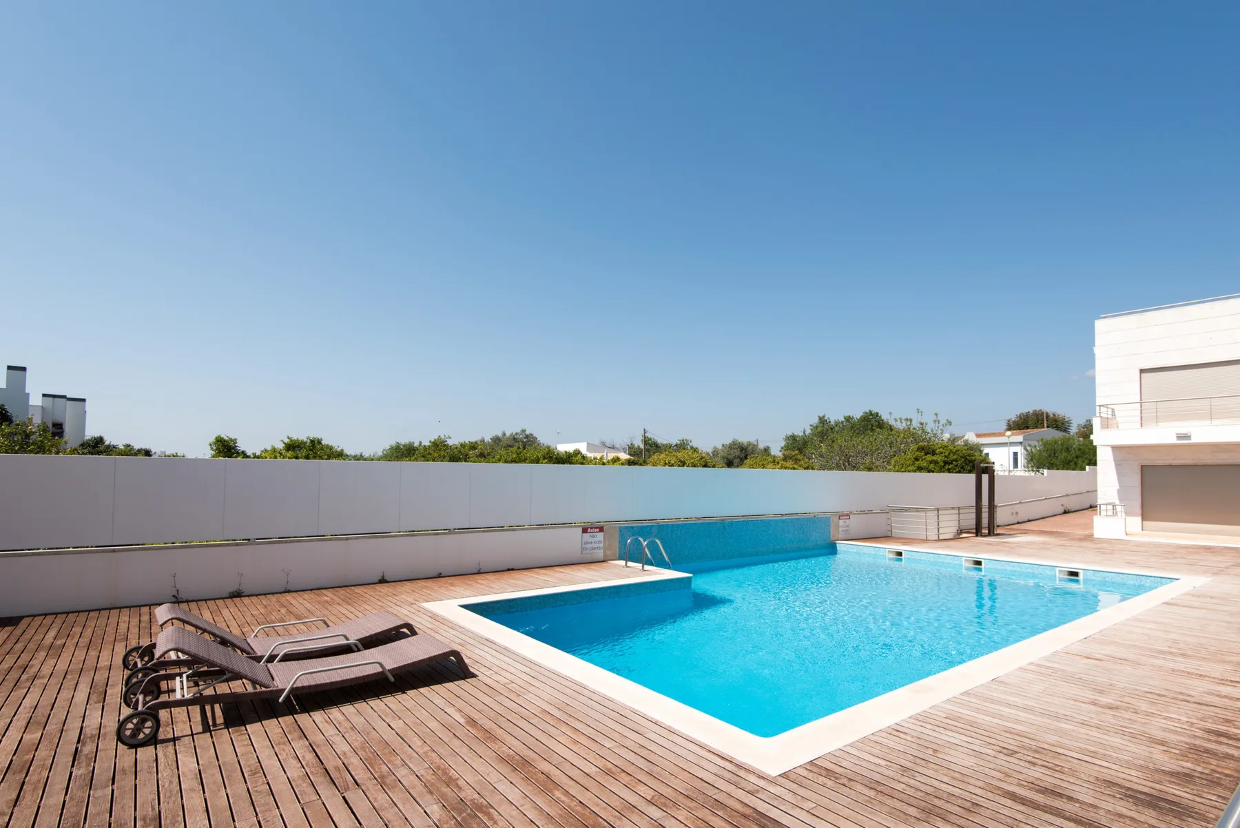 An outdoor swimming pool sits beside a wooden deck with lounge seating.