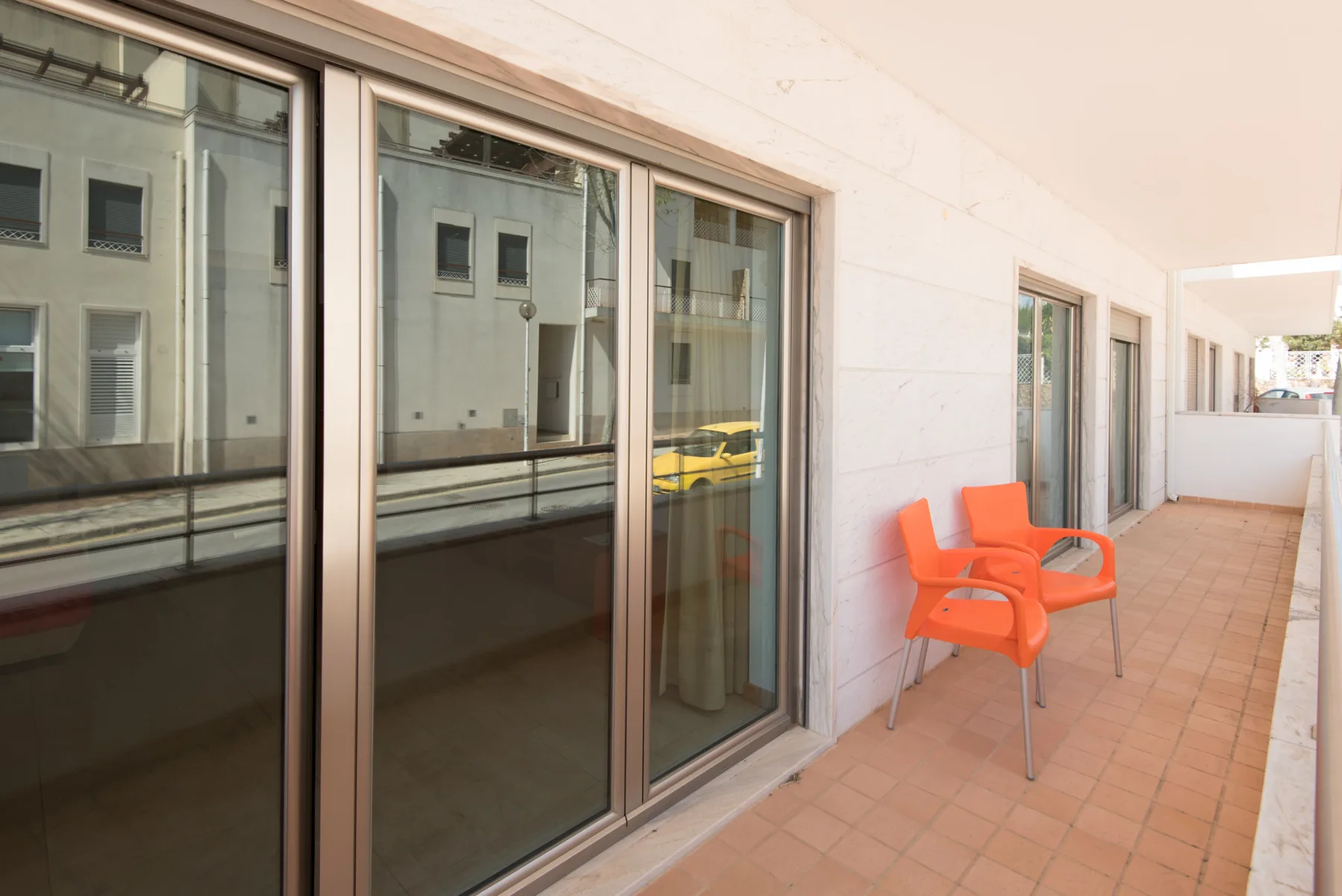 A tiled balcony corridor with sliding glass doors and orange seating.