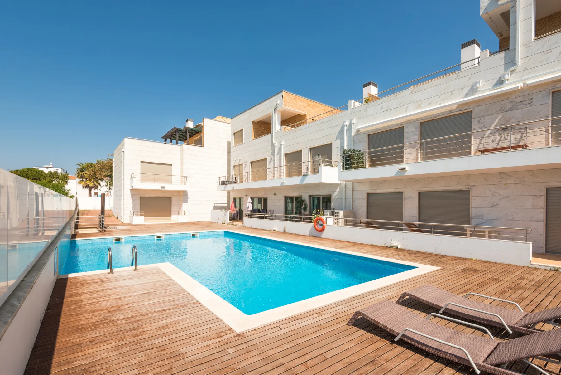 Una piscina al aire libre está junto a un edificio de apartamentos moderno y una terraza de madera.