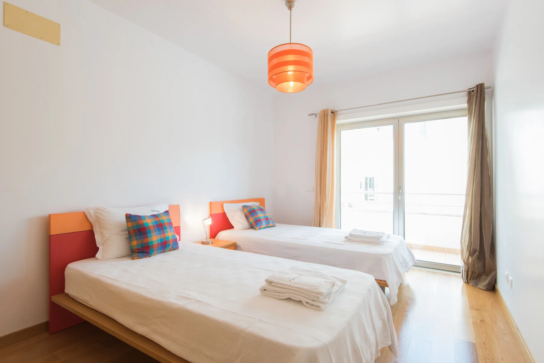 A bright bedroom has two beds beside a large window.