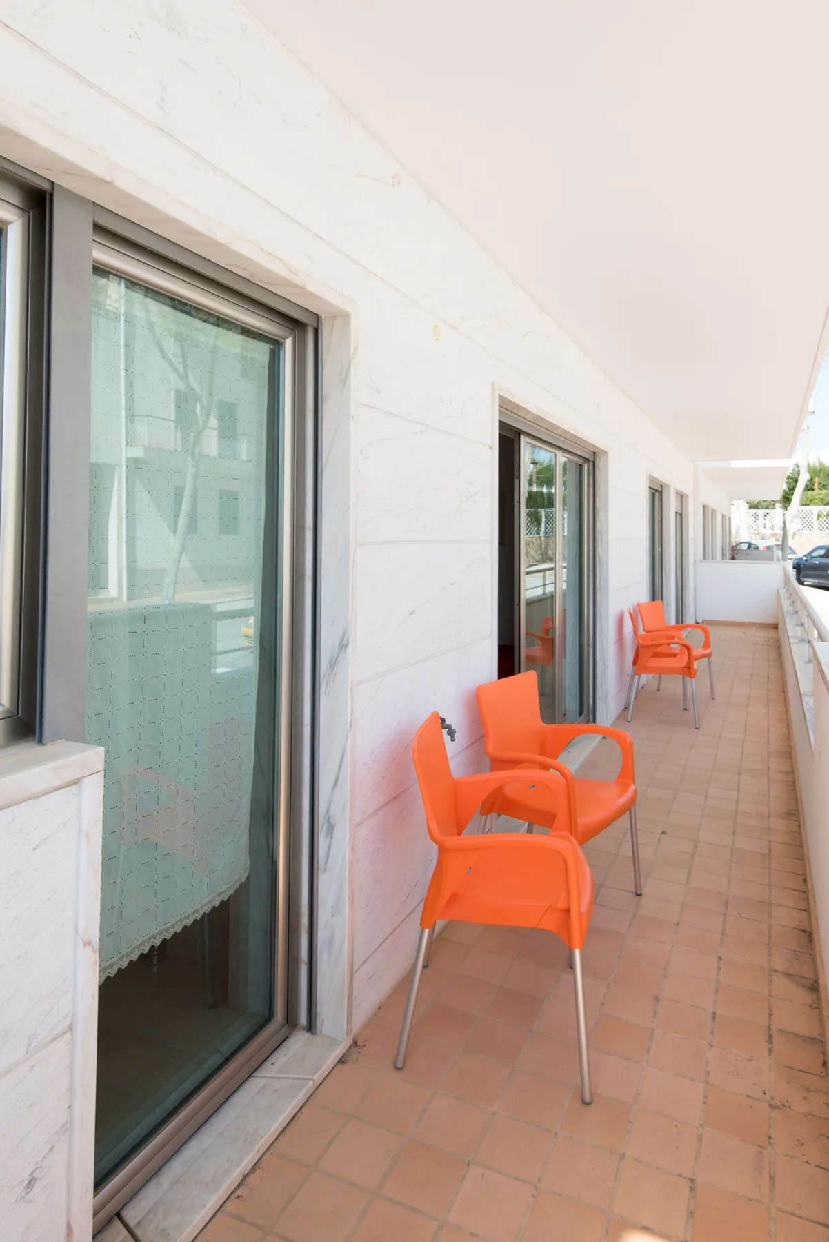A tiled outdoor walkway runs beside windows and orange seating.