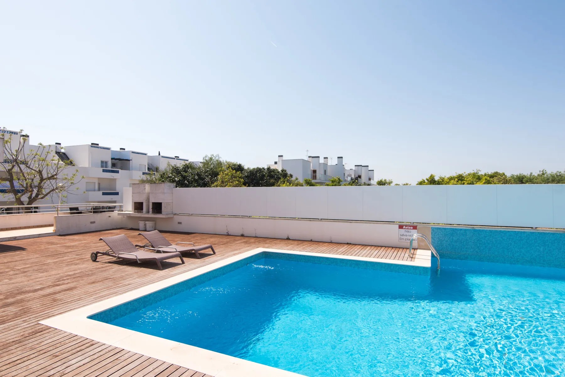 An outdoor swimming pool beside a wooden deck and lounge seating.