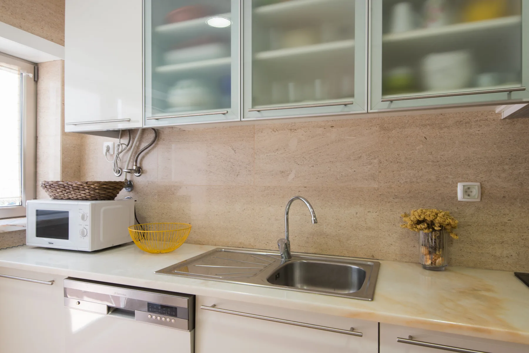 A bright kitchen with a sink, countertop, and upper cabinets.