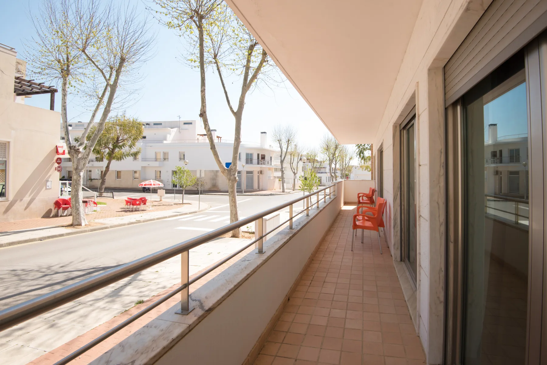 A balcony walkway with tiled flooring, railing, and outdoor seating.