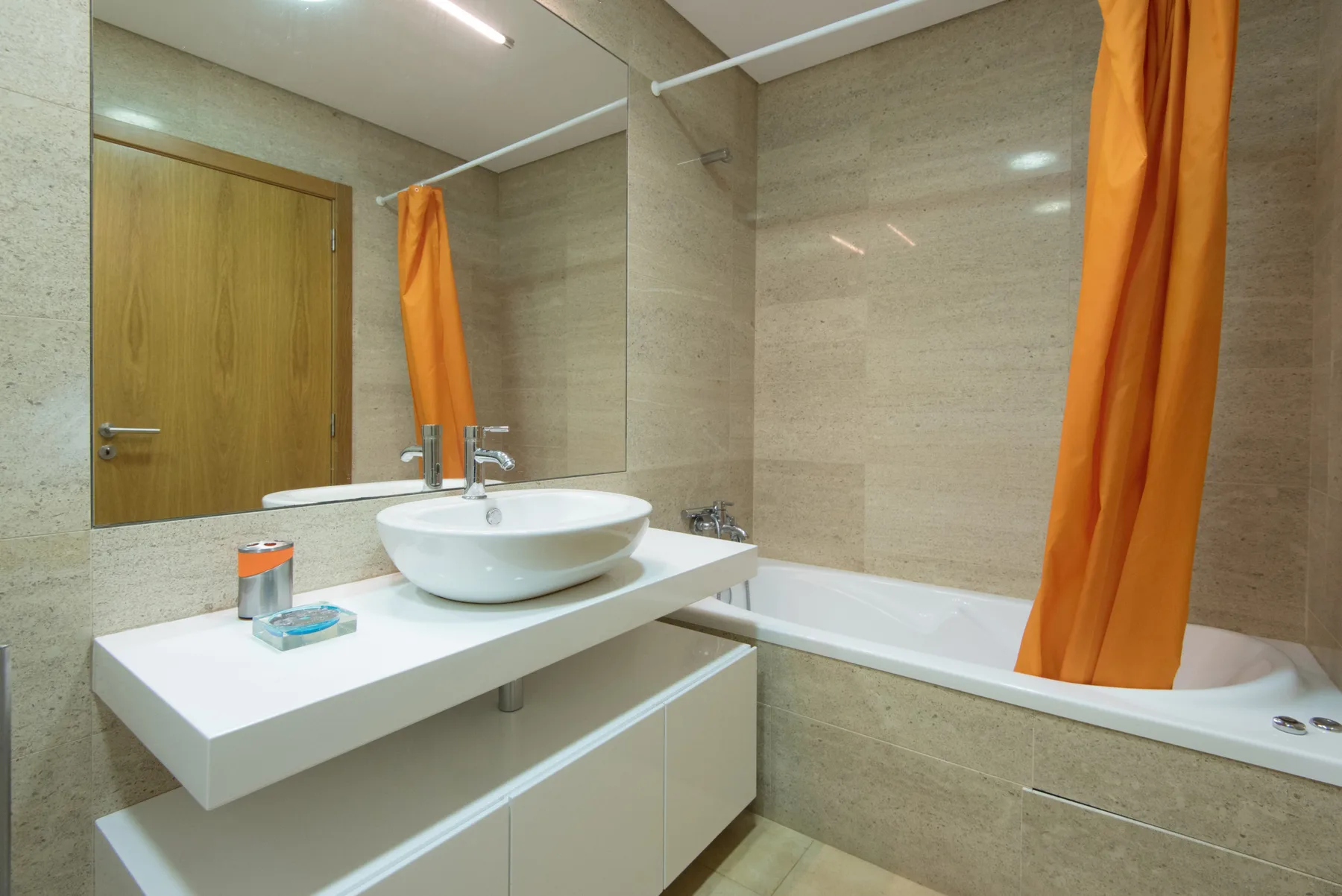 A bathroom with a sink beside a bathtub and orange curtains.