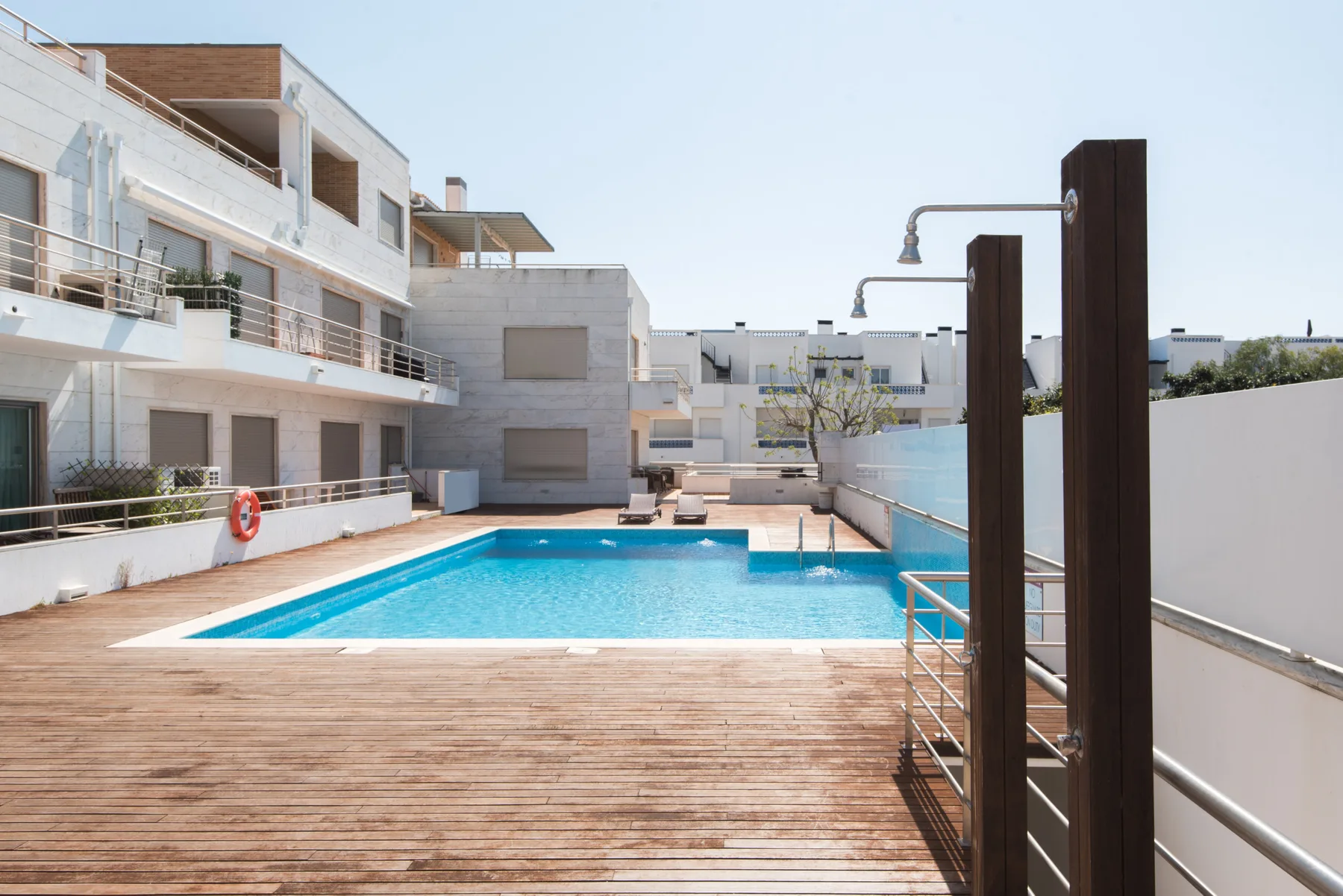 An outdoor swimming pool sits beside modern buildings and a wooden deck.