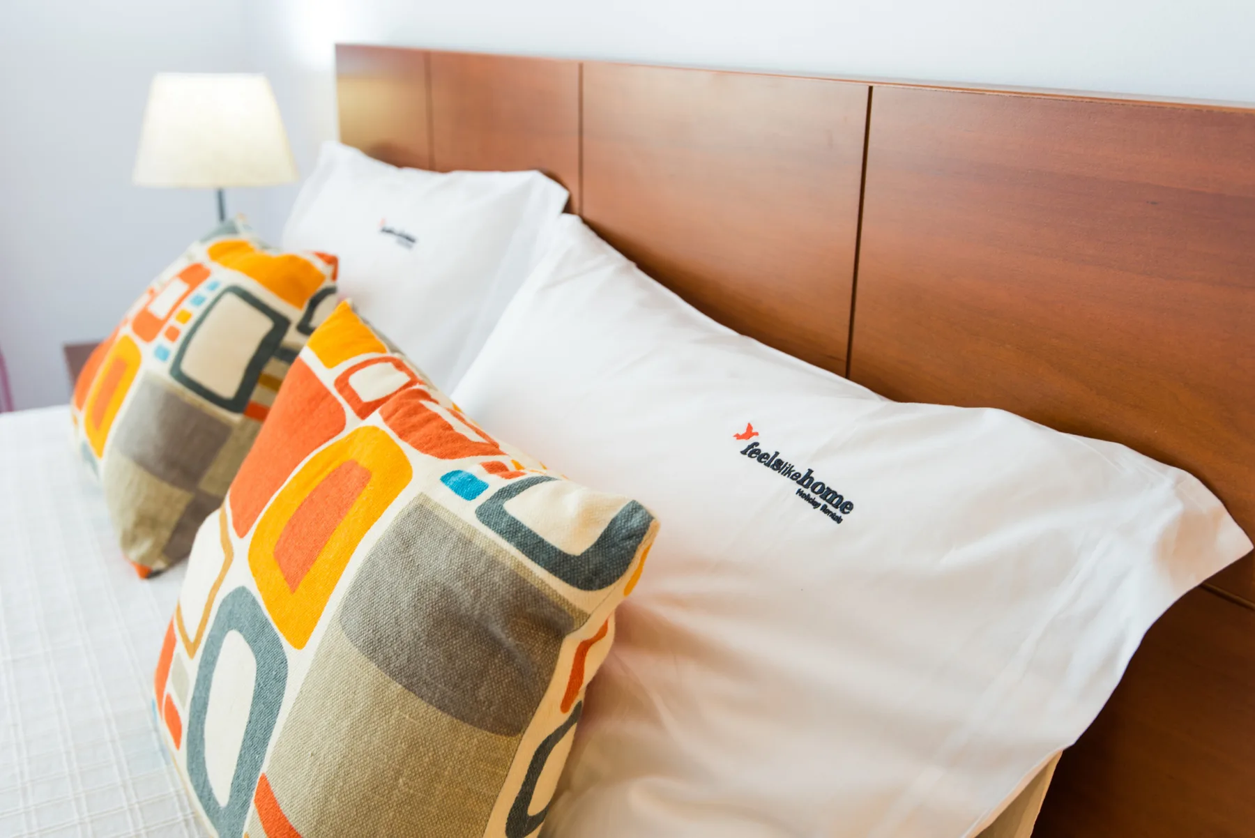 A bedroom bed with white bedding and colorful patterned cushions.