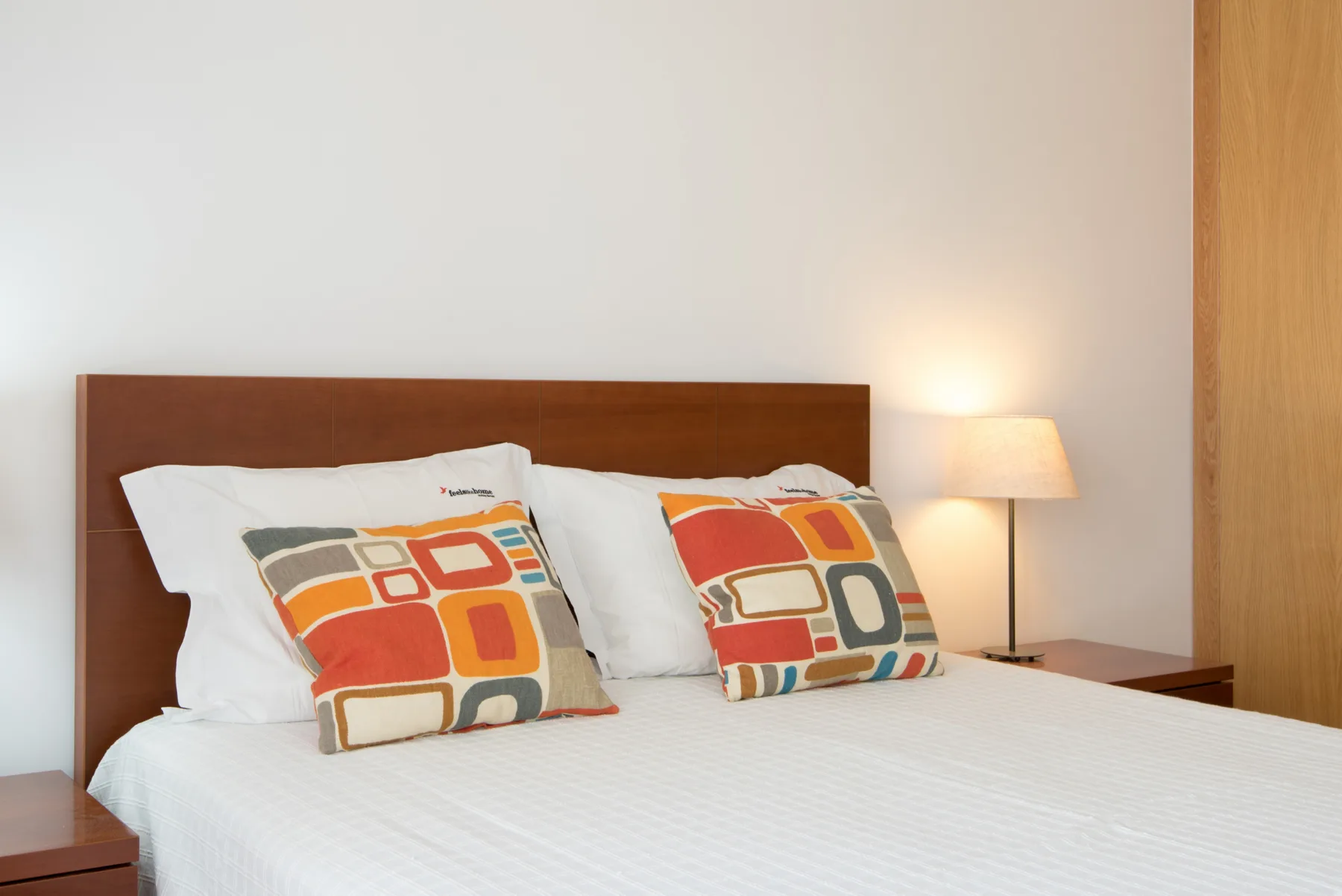A bedroom with a bed, colorful patterned pillows, and a bedside lamp.