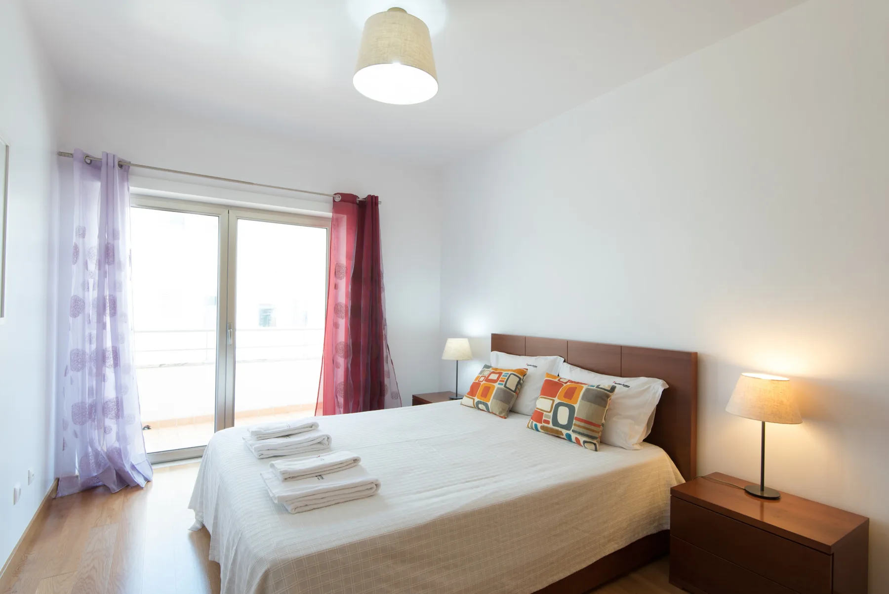 A bright bedroom with a double bed and colorful accent pillows.