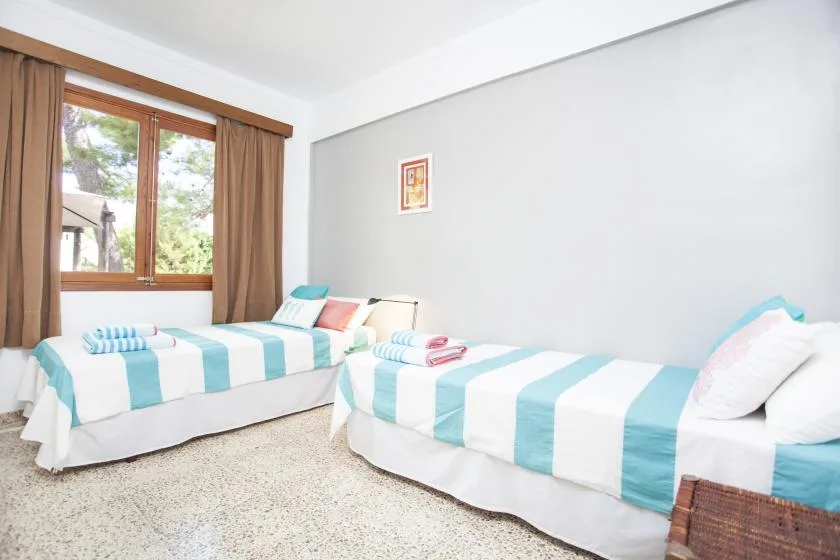 Un dormitorio con dos camas vestidas con ropa de rayas azules y blancas junto a una ventana.