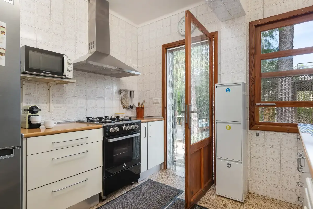 Una cocina alicatada con cocina, microondas y una puerta de madera abierta.