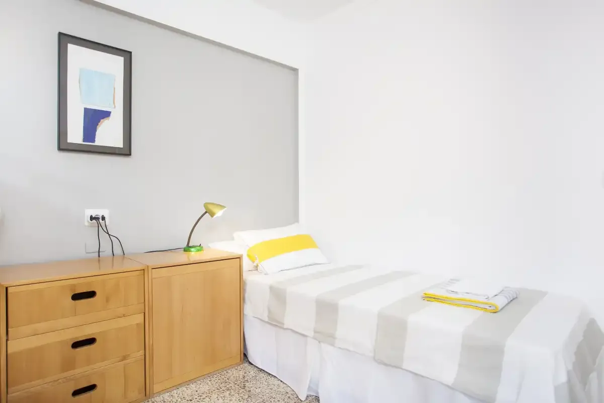 Un dormitorio con una cama individual, una cómoda de madera y un cuadro enmarcado.