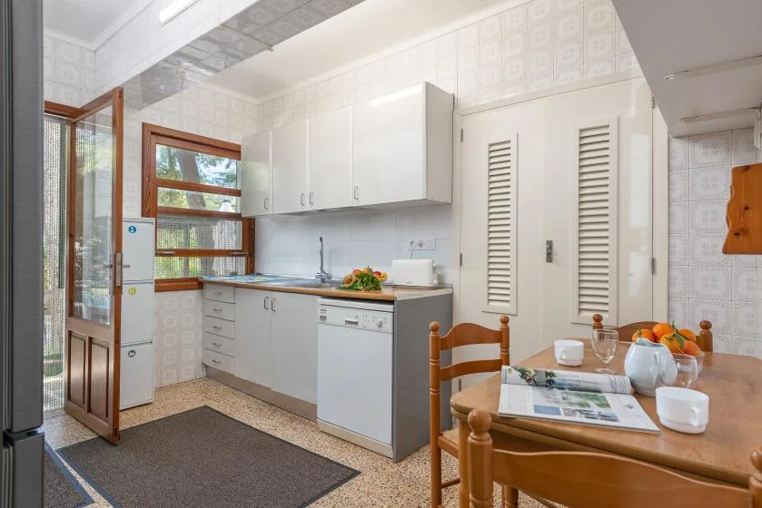 Una cocina luminosa con gabinetes blancos, una encimera y una pequeña mesa de comedor.