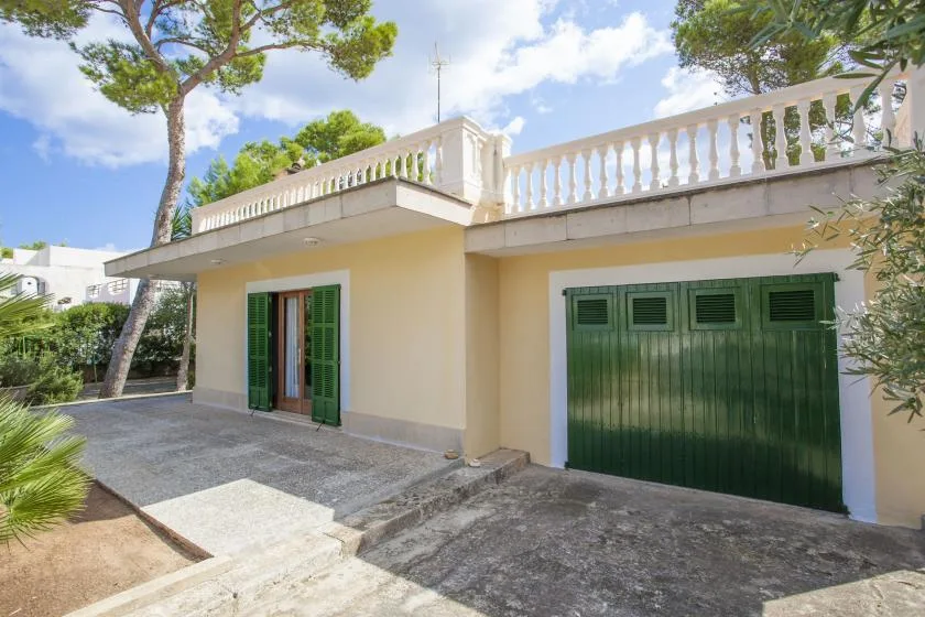 Exterior de una casa clara con contraventanas verdes, puerta de garaje y terraza en la azotea.