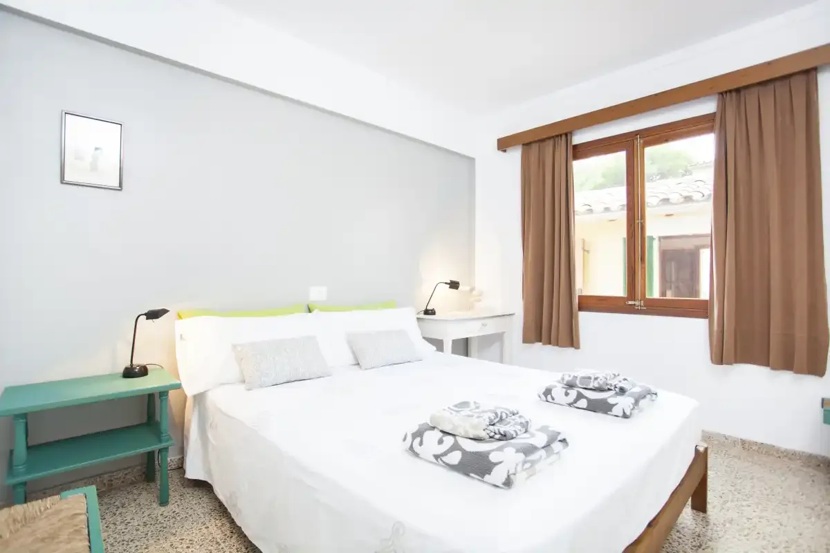 Un dormitorio luminoso con una cama blanca y una ventana grande.
