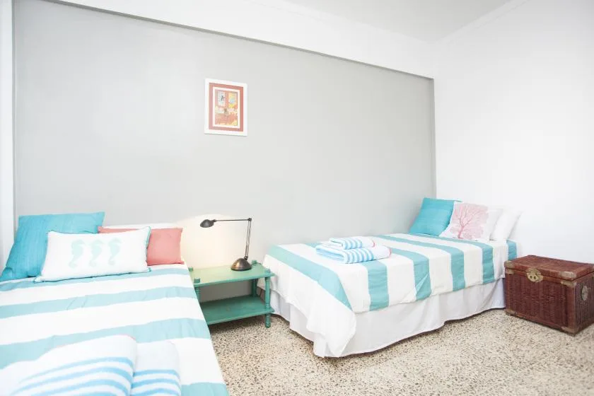 Un dormitorio luminoso con dos camas vestidas de blanco y turquesa.