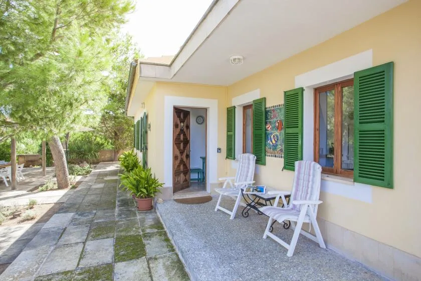 Un patio junto a una casa amarilla, con asientos al aire libre y contraventanas verdes.