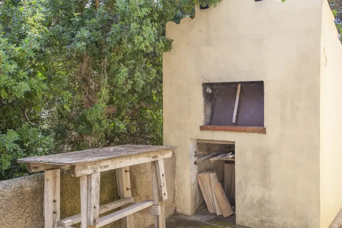 Una zona de cocina exterior con una mesa de trabajo rústica junto a una pared enlucida.